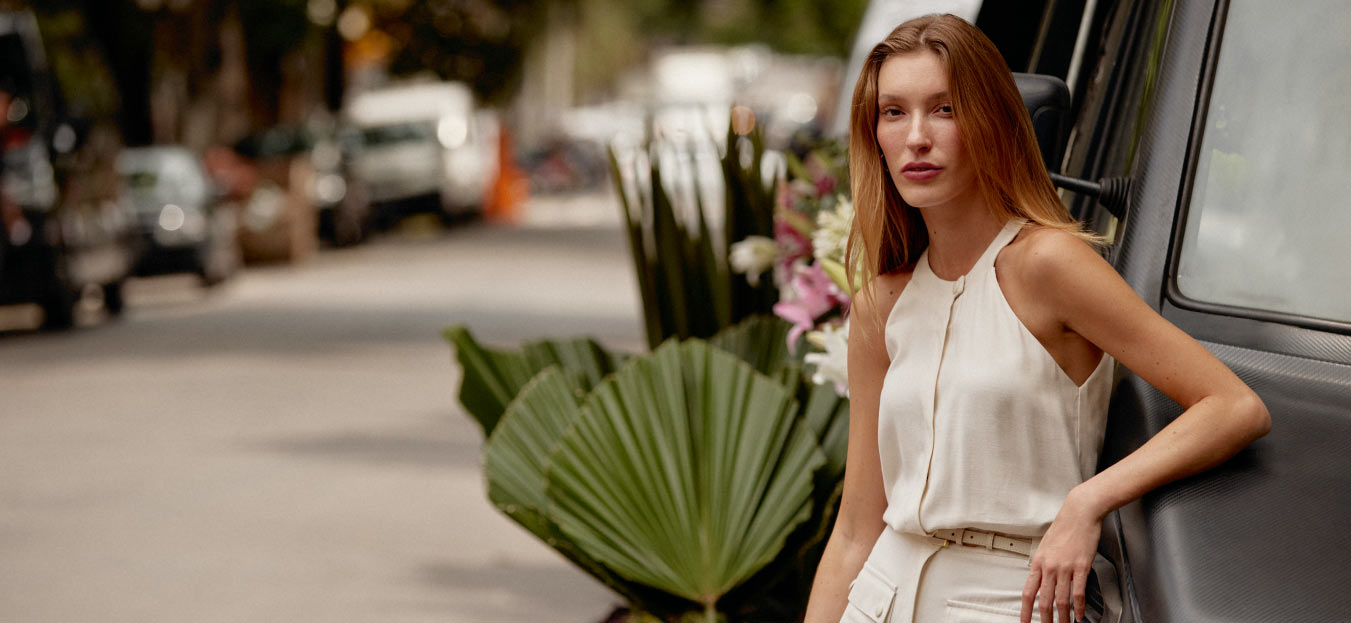 modelo posando com blusas e calça de alfaiataria branca representando tendências para verão